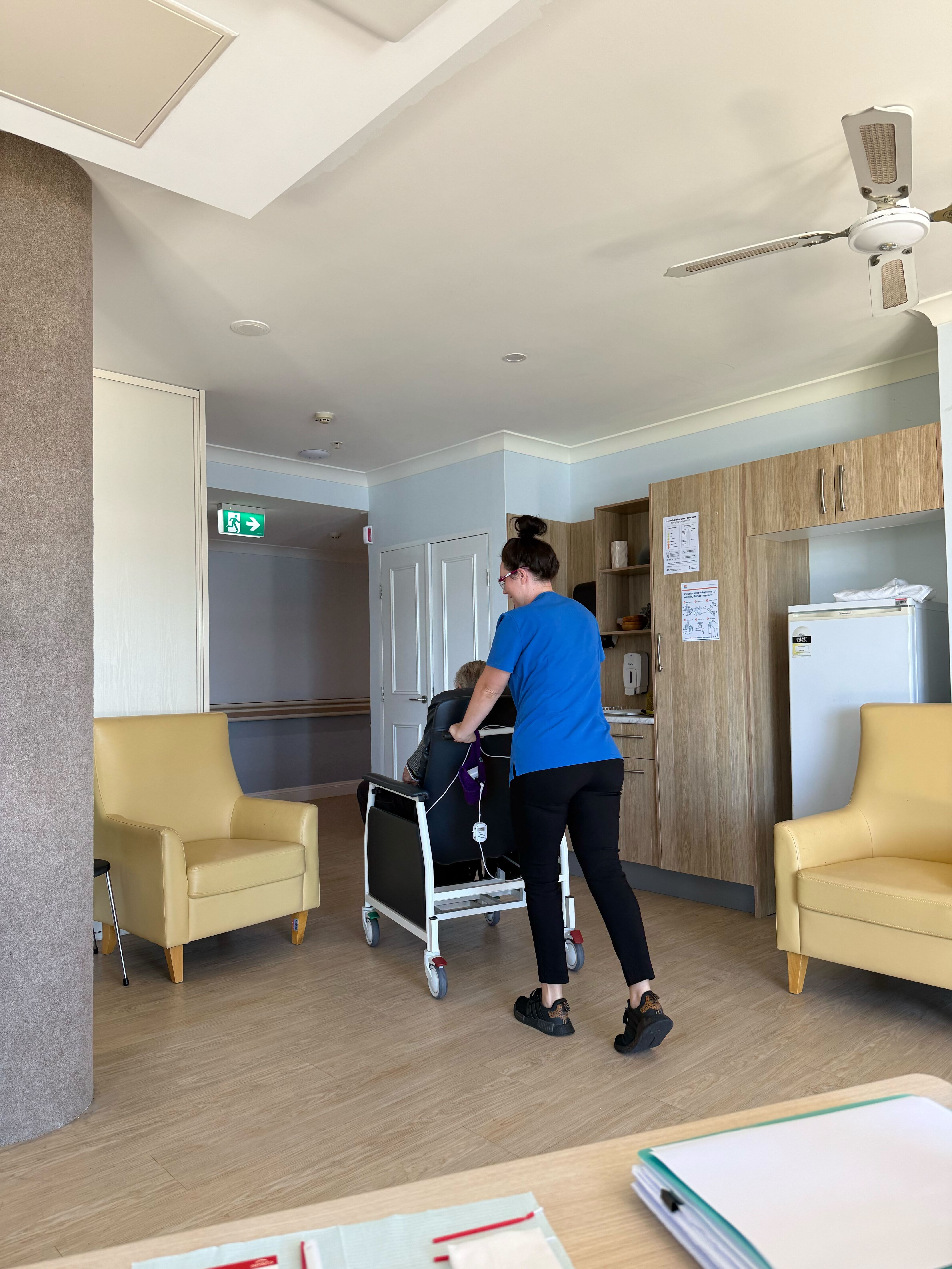 Oral health therapist wheeling portable dental chair through an aged care facility corridor